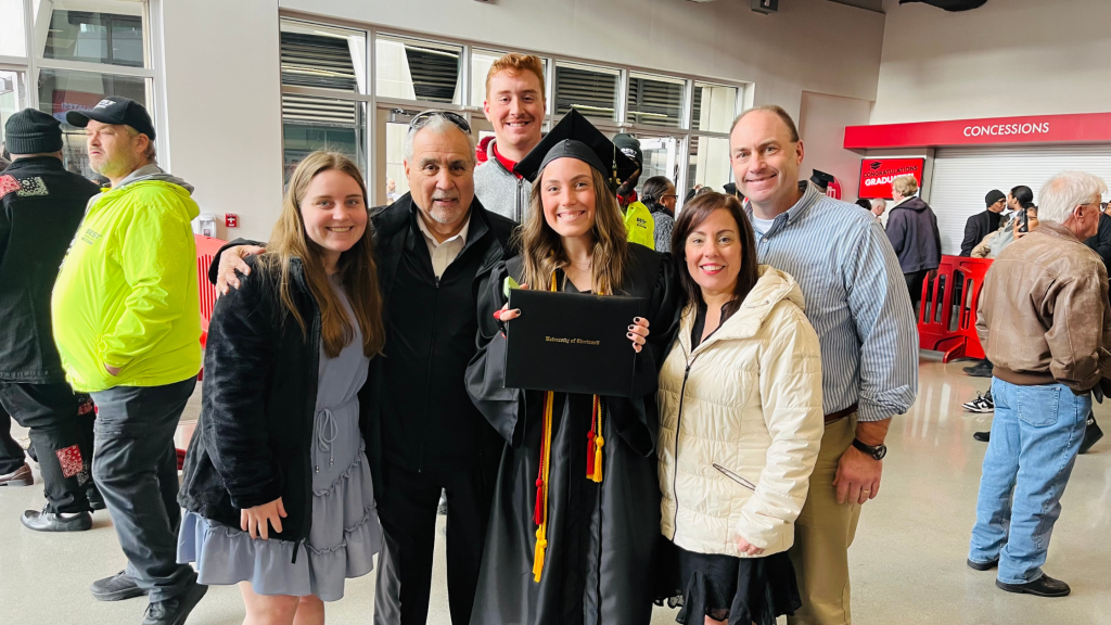 Emily holding up her college diploma with and her family at her college graduation