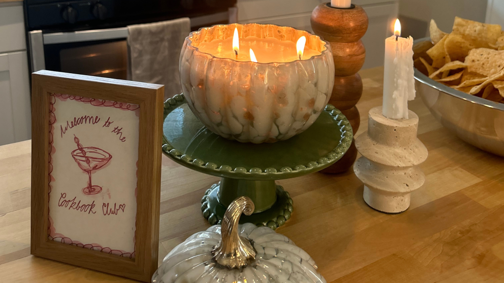 Kitchen island with a lit pupkin candle, two lit candle sticks, a bowl of tortillas and a sign that reads welcome to the cookbook club.