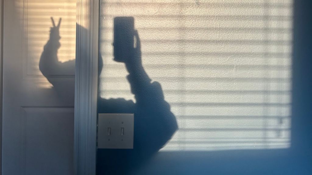 silhouette of a girl making a peace sign taking a picture with her phone in the morning light