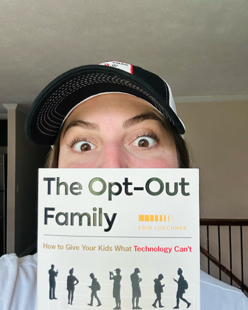 Close up of Emily in a hat holding The Opt-Out Family book by Erin Loechner over her mouth. 